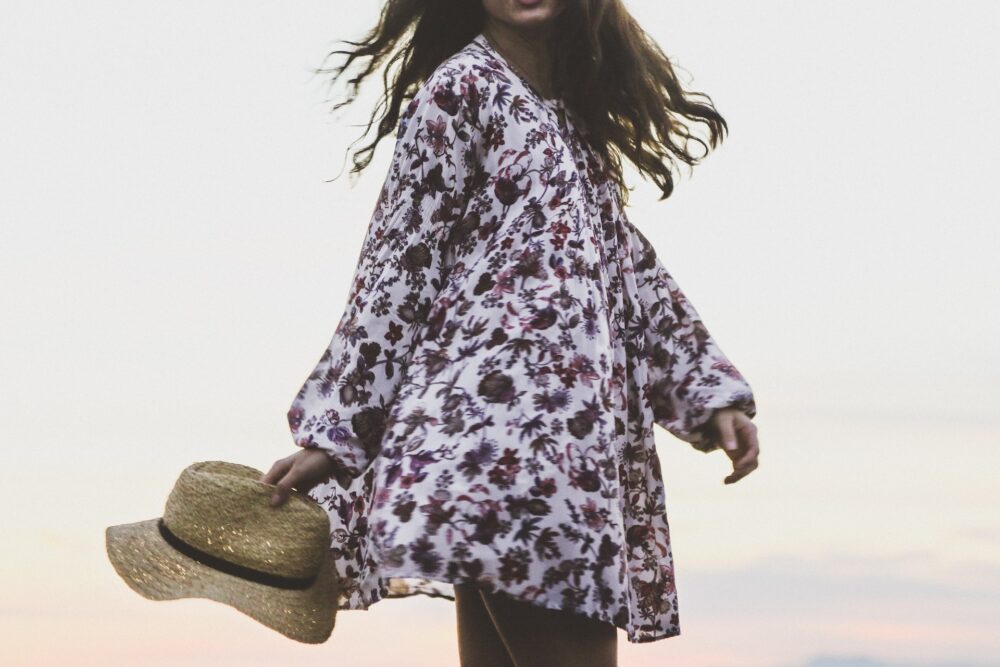 woman wearing white and brown floral long-sleeved shirt while holding hat